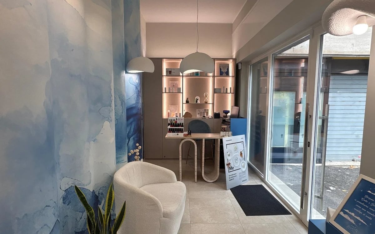Modern bathroom showroom with white vanity, blue accent wall, shelving, and glass doors leading to outdoor area