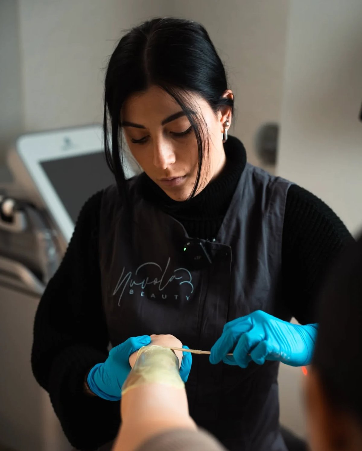Esthetician in black uniform and blue gloves applying treatment to clients arm in beauty salon