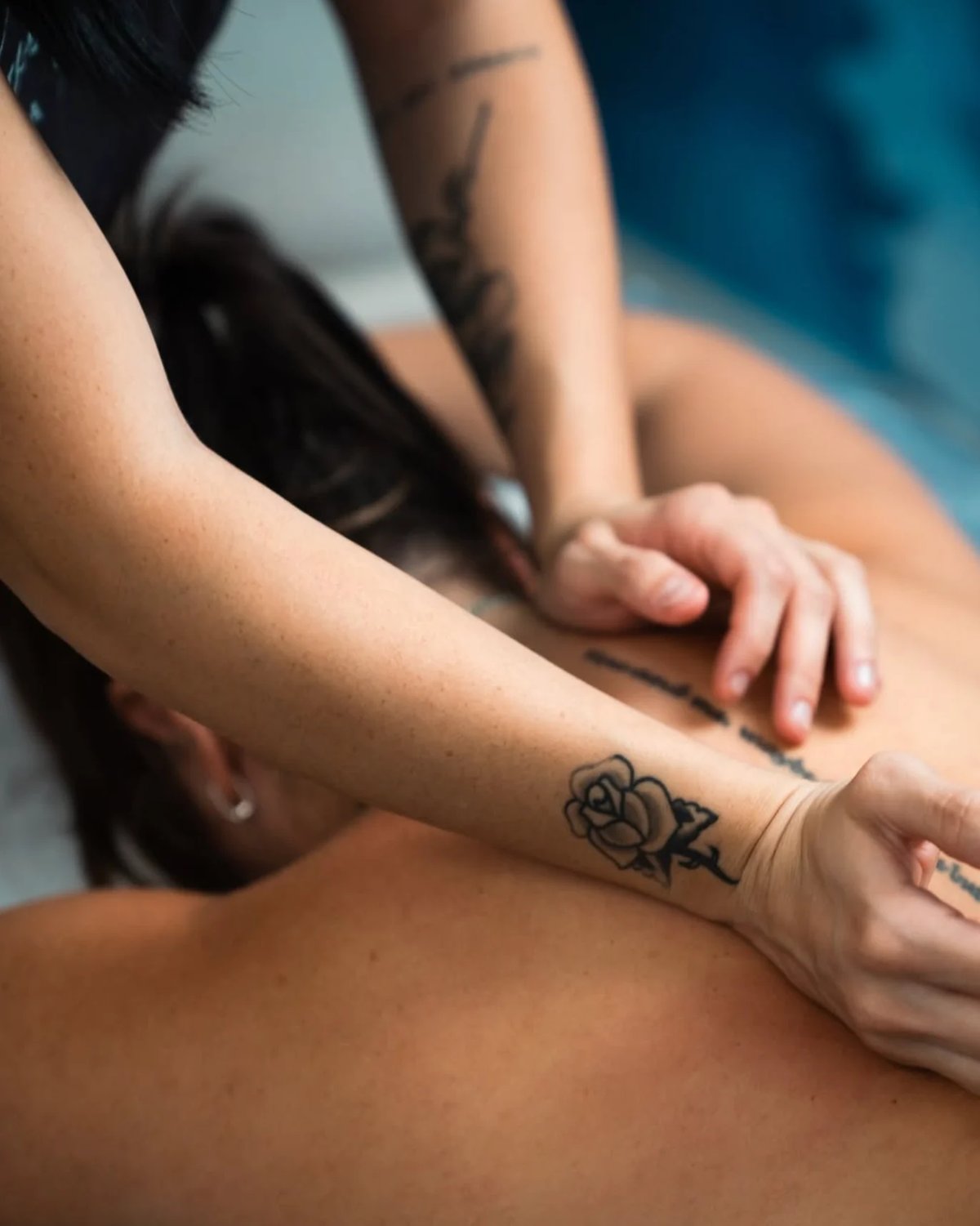 Person with rose tattoo on wrist receiving a massage or therapeutic touch on their arm and shoulder