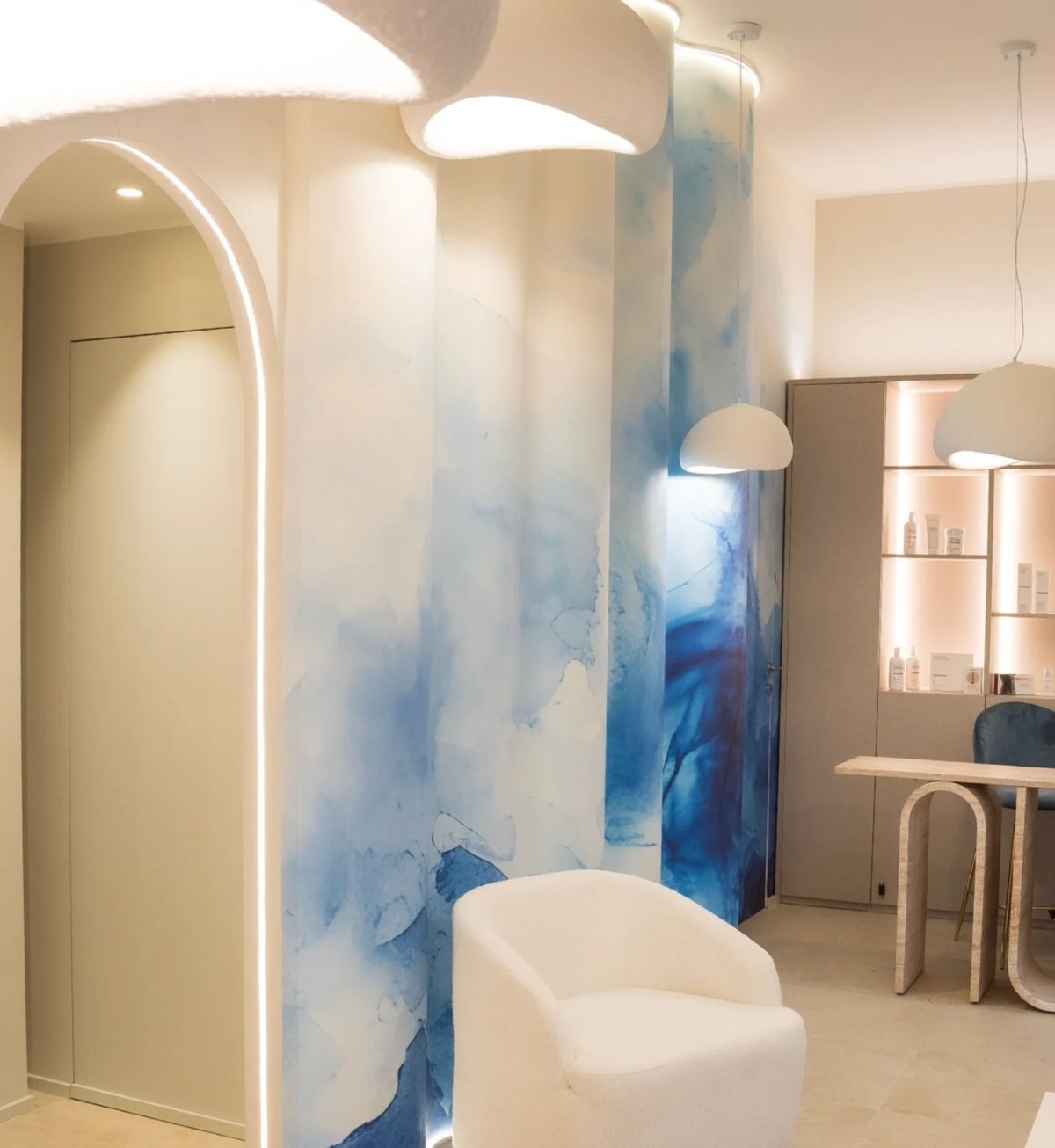 Modern bathroom with blue and white watercolor-style partition wall, white curved fixtures, pendant lighting, and minimalist design